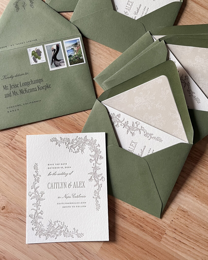 Elegant letterpress save the date cards for Caitlyn and Alex’s 2024 wedding in Napa, California, featuring floral border illustrations and sage green envelopes with printed guest addresses and vintage stamps. This stationery suite is designed with attention to detail, including envelope liners and showcases current 2025 USPS postage rates.